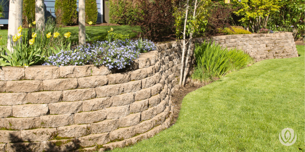 Stacked stone retaining wall with lush greenery and flowerbeds