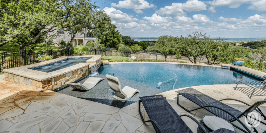 Luxury freeform pool overlooking a lake with stone patio and lounge seating