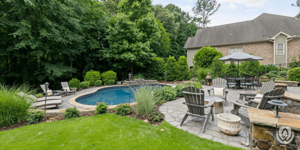 Curved backyard pool with surrounding patio, fire pit seating, landscaping, and outdoor dining area