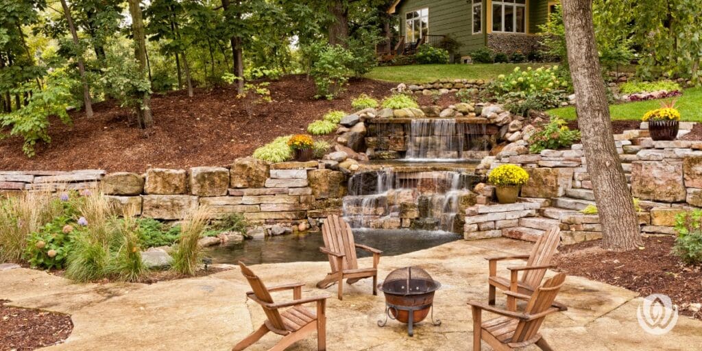 Luxury patio with wooden chairs arranged around a decorative stone water feature and colorful garden plantings